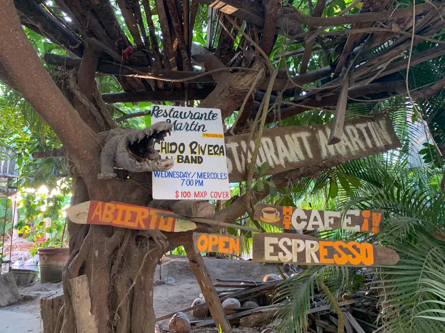 Hand-painted signs beneath a tropical canopy advertise coffee, food and live music at a favorite village gathering spot.