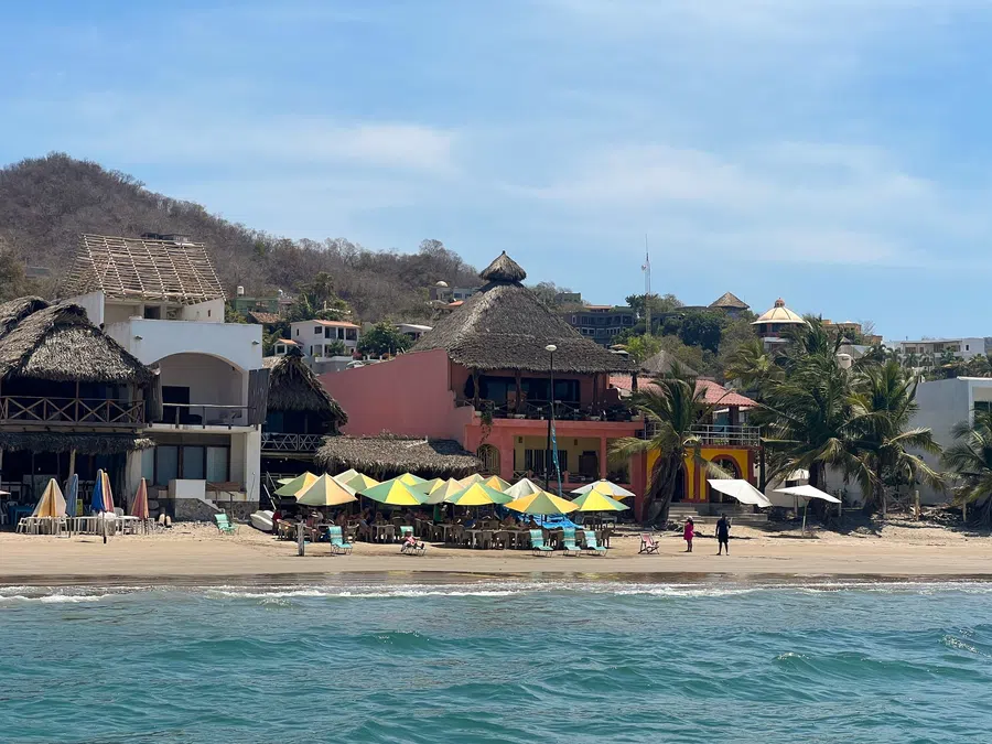 Colorful umbrellas and open-air restaurants line the shore beneath the hills of La Manzanilla.
