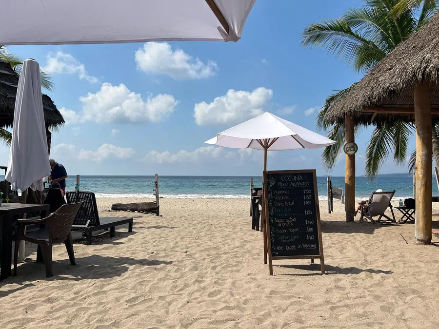 Open-air tables, palapa shade and white umbrellas sit directly on the sand with the Pacific just steps away.
