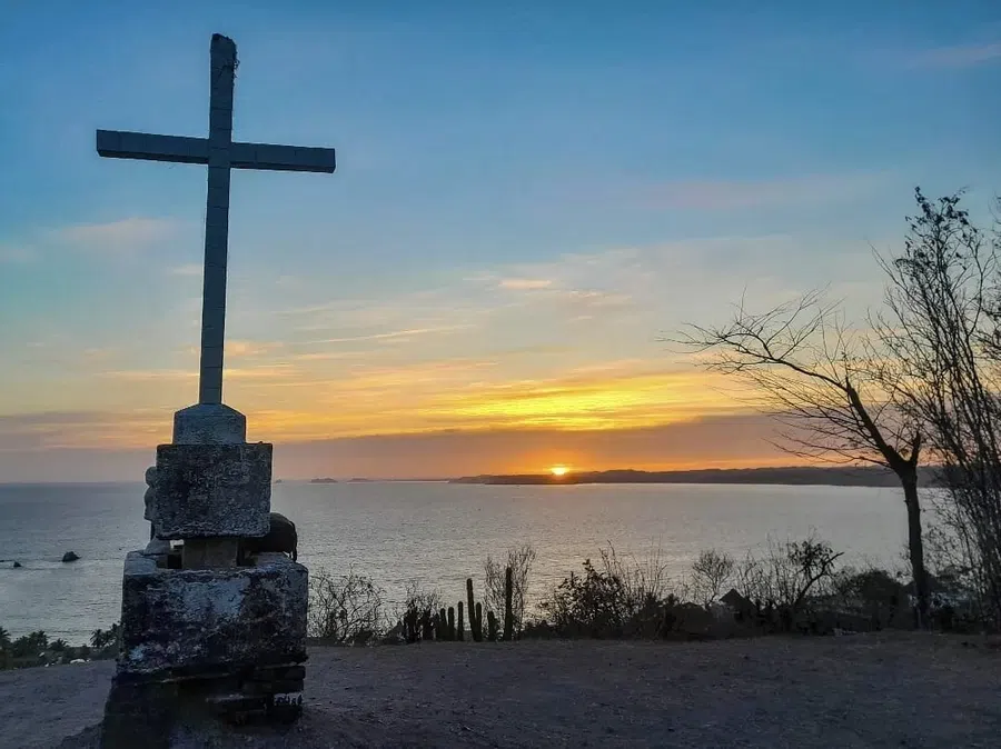A hilltop cross is silhouetted against the last light over the Pacific.