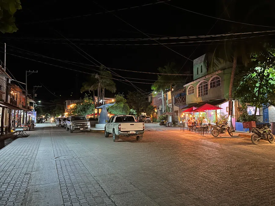 Restaurants and storefronts cast warm light along the village's broad central street.