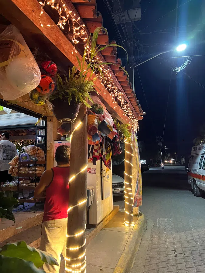 A small local shop wrapped in warm string lights adds to the village's informal nighttime charm.