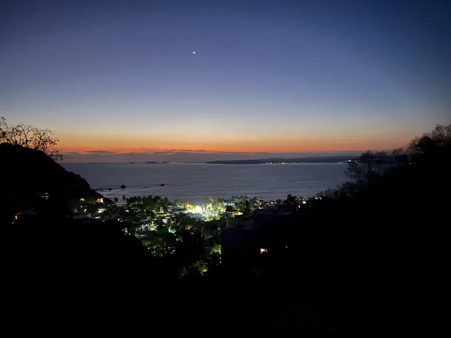 Elevated evening view captures the village lights below and the fading glow over the Pacific.
