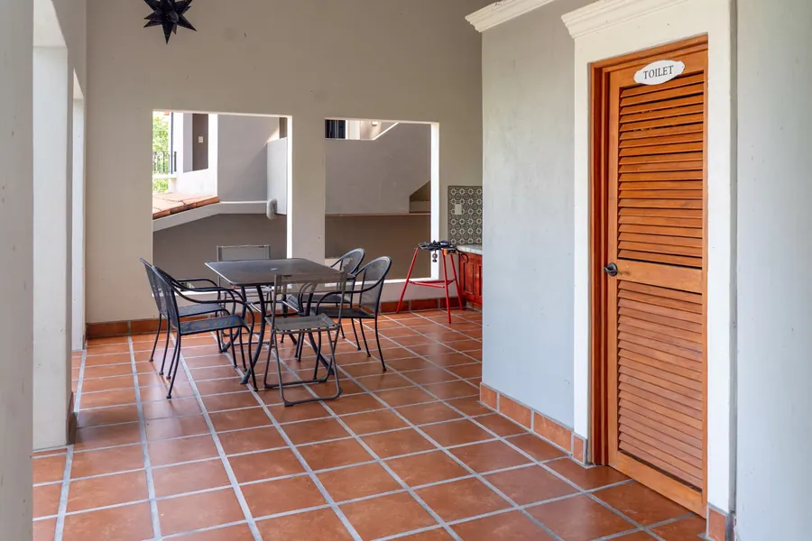 Covered outdoor kitchen and dining area of the main residence, adjoining the outdoor hallway, with terracotta tile, dining table and a convenient poolside half bath.