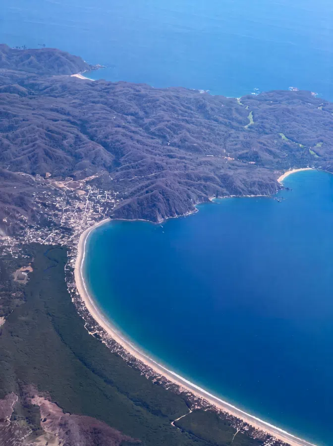 Aerial view of the Costalegre coastline, with the long sweep of the bay and rugged green hills meeting the Pacific.