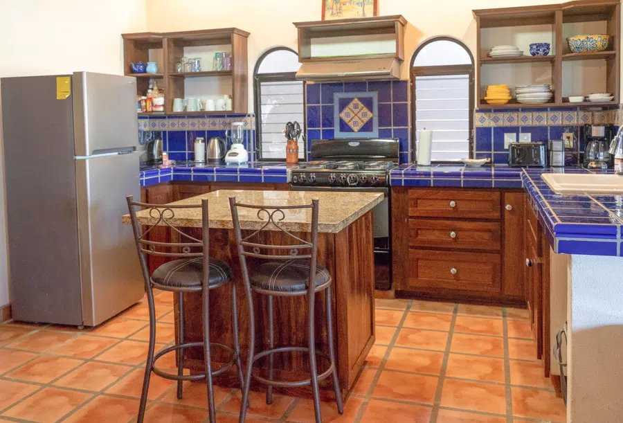 Full kitchen with blue tile counters, wood cabinetry, island seating and a full-size refrigerator.