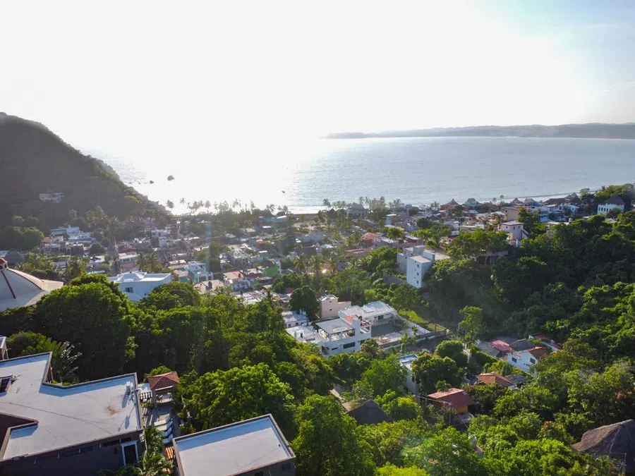 Elevated aerial view across La Manzanilla toward the broad curve of the Pacific coastline.