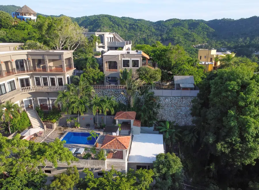 Aerial view showing the residence, pool and gardens tucked into the green hillside above La Manzanilla.