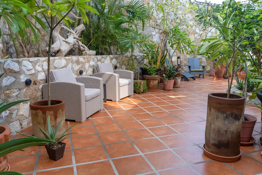 A secluded tiled patio with comfortable seating and mature tropical landscaping.