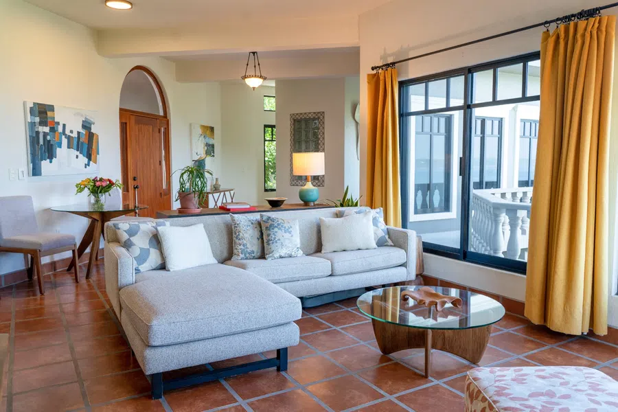 Comfortable main-house living room with generous windows, warm tile floors and direct connection to the balcony.