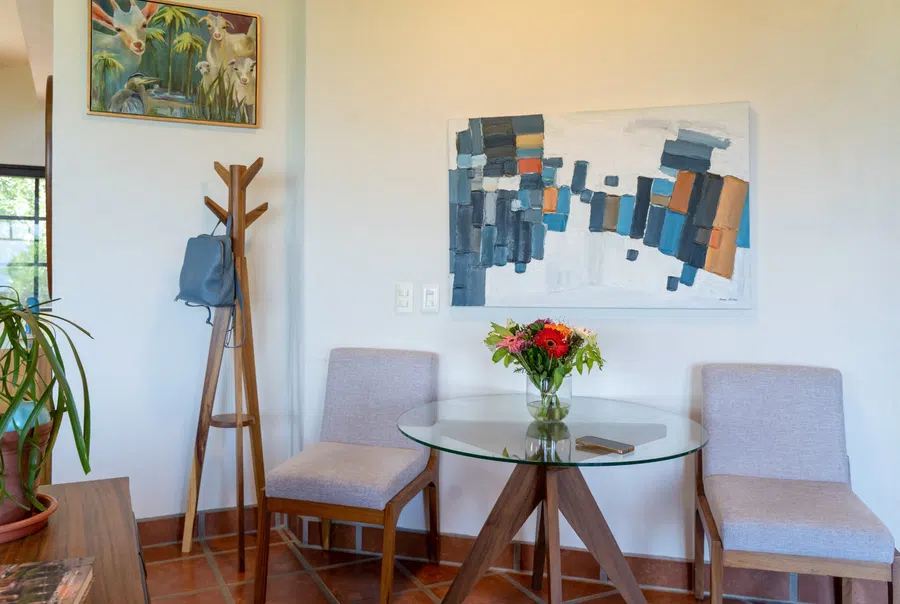 Intimate glass-top dining table beneath original artwork in the main residence.