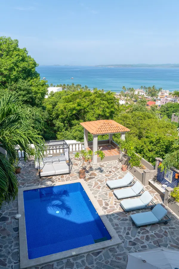 Vertical view of the blue-tiled pool, sun deck and ocean beyond.