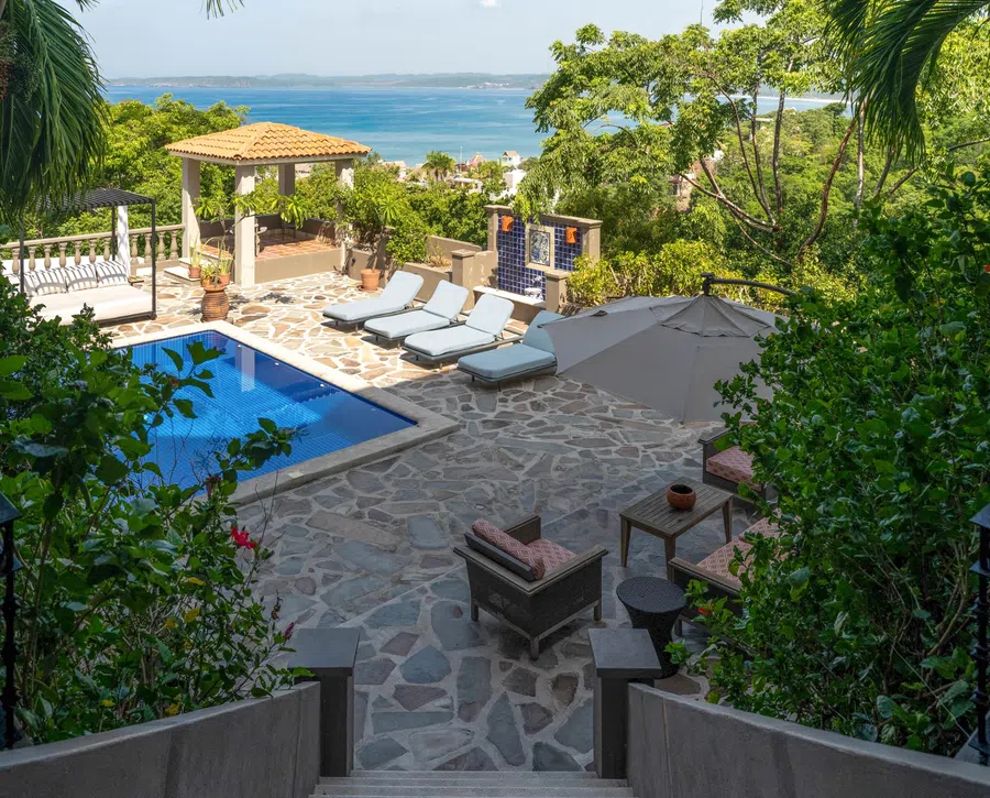 Terrace view down across the pool deck with the bay visible beyond the trees.
