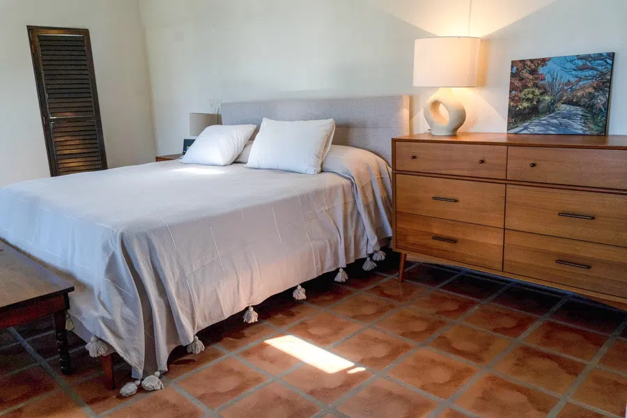 Bright bedroom with king-sized bed, wood dresser and terracotta tile floors. En suite bathroom not pictured here.