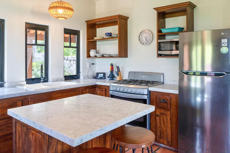 Full-size kitchen with stone-topped island, wood cabinetry and stainless refrigerator.