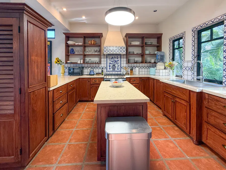 Wide-angle view of the main kitchen with center island, wood cabinetry and Mexican tile.