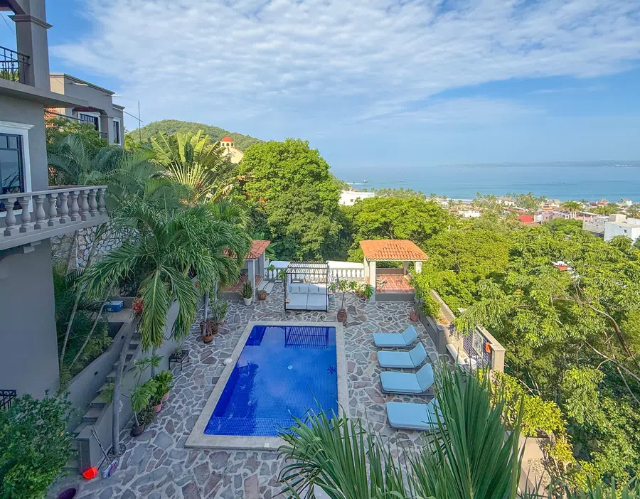 Wide view of the pool deck framed by palms and hillside greenery.